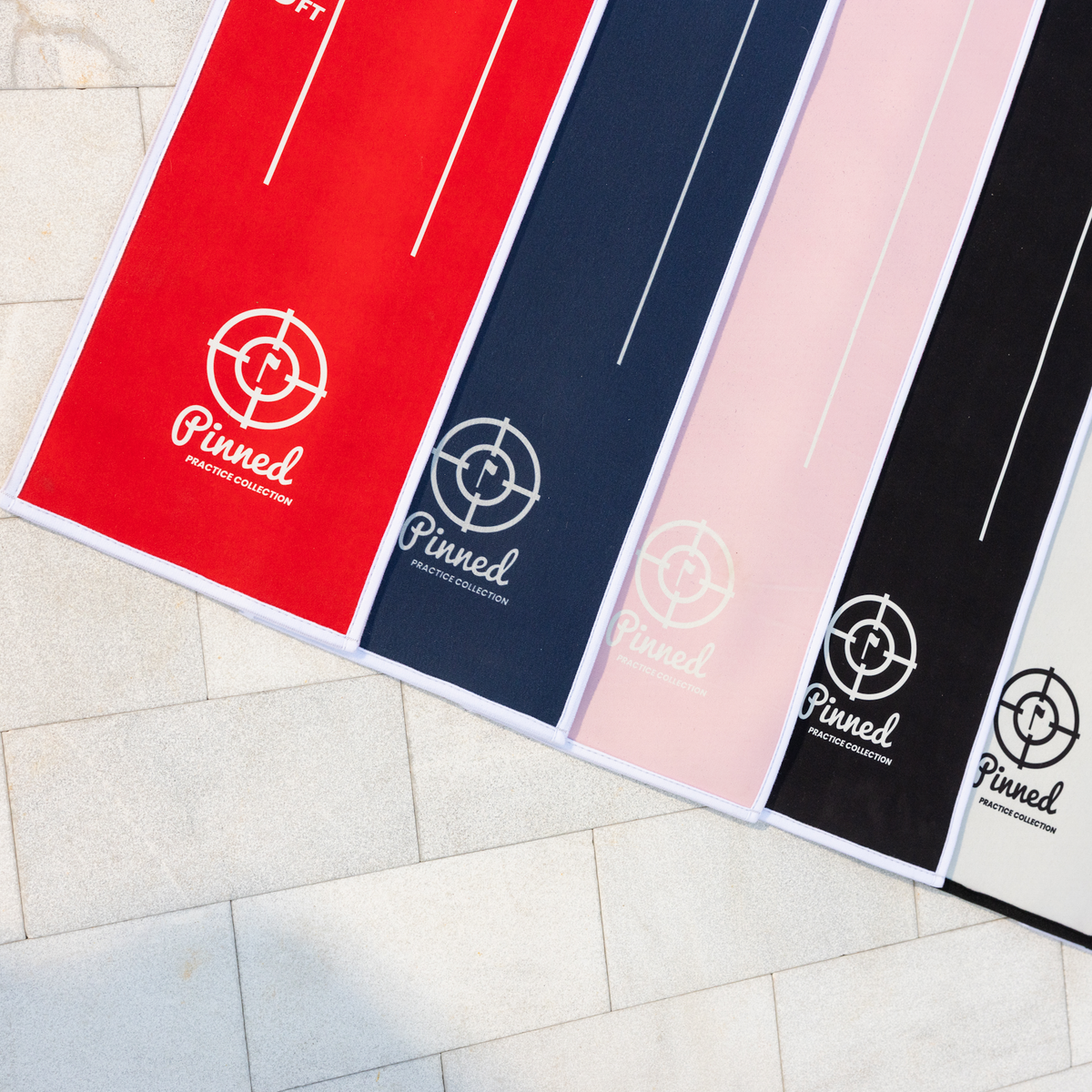Various putting mats of an assortment of colors with the 'Pinned' branding on each layered on the ground