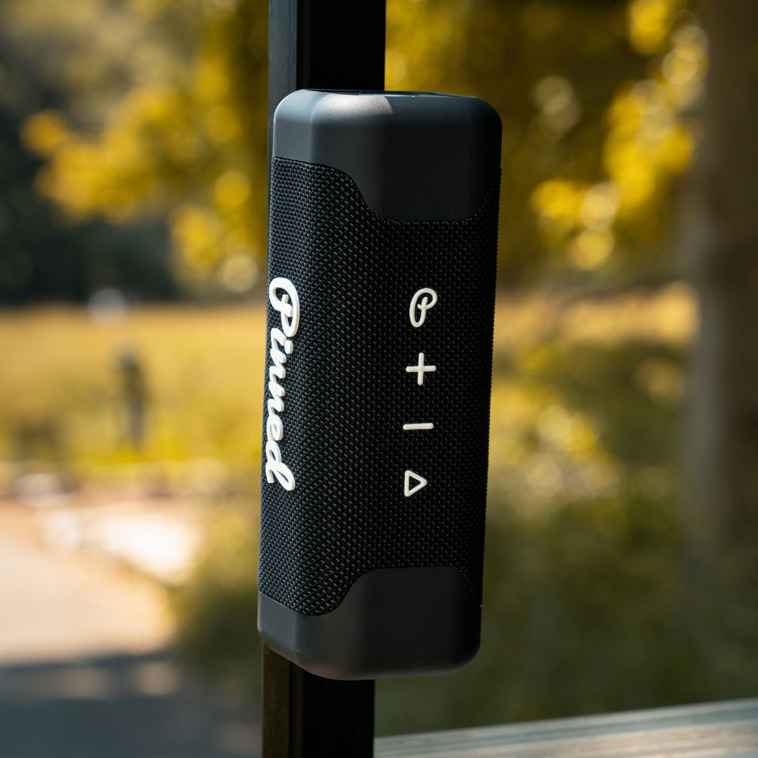 Black portable speaker with 'Pinned' branding in white magnetically attached to a golf cart