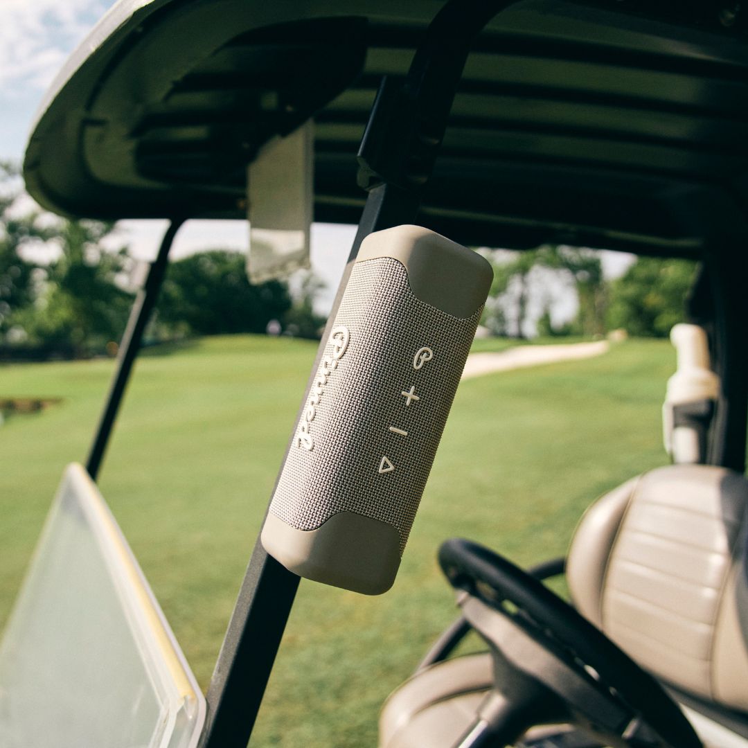 Gray portable speaker with 'Pinned' branding in white magnetically attached to a golf cart