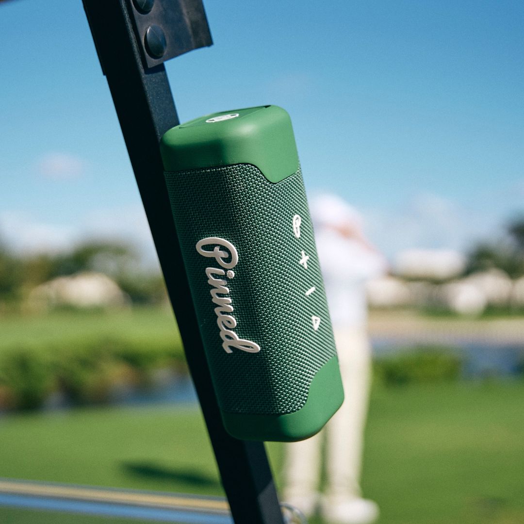 Green portable speaker with 'Pinned' branding in white magnetically attached to a golf cart