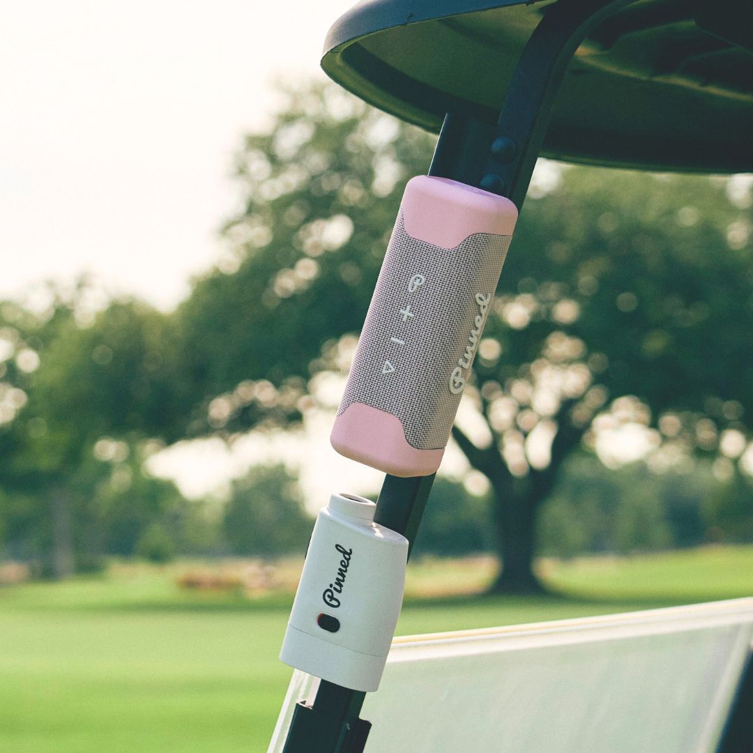 Pink portable speaker with 'Pinned' branding in white magnetically attached to a golf cart