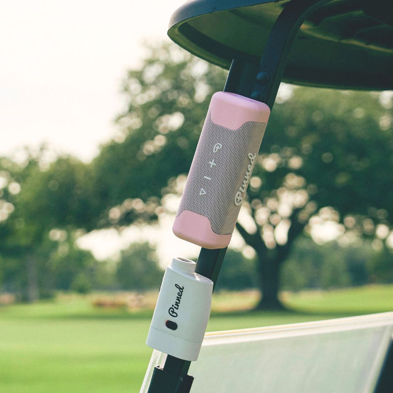 Pink portable speaker with 'Pinned' branding in white magnetically attached to a golf cart