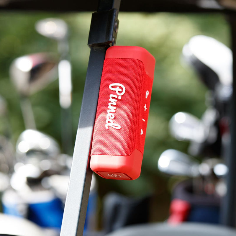 Red portable speaker with 'Pinned' branding magnetically attached to a golf cart